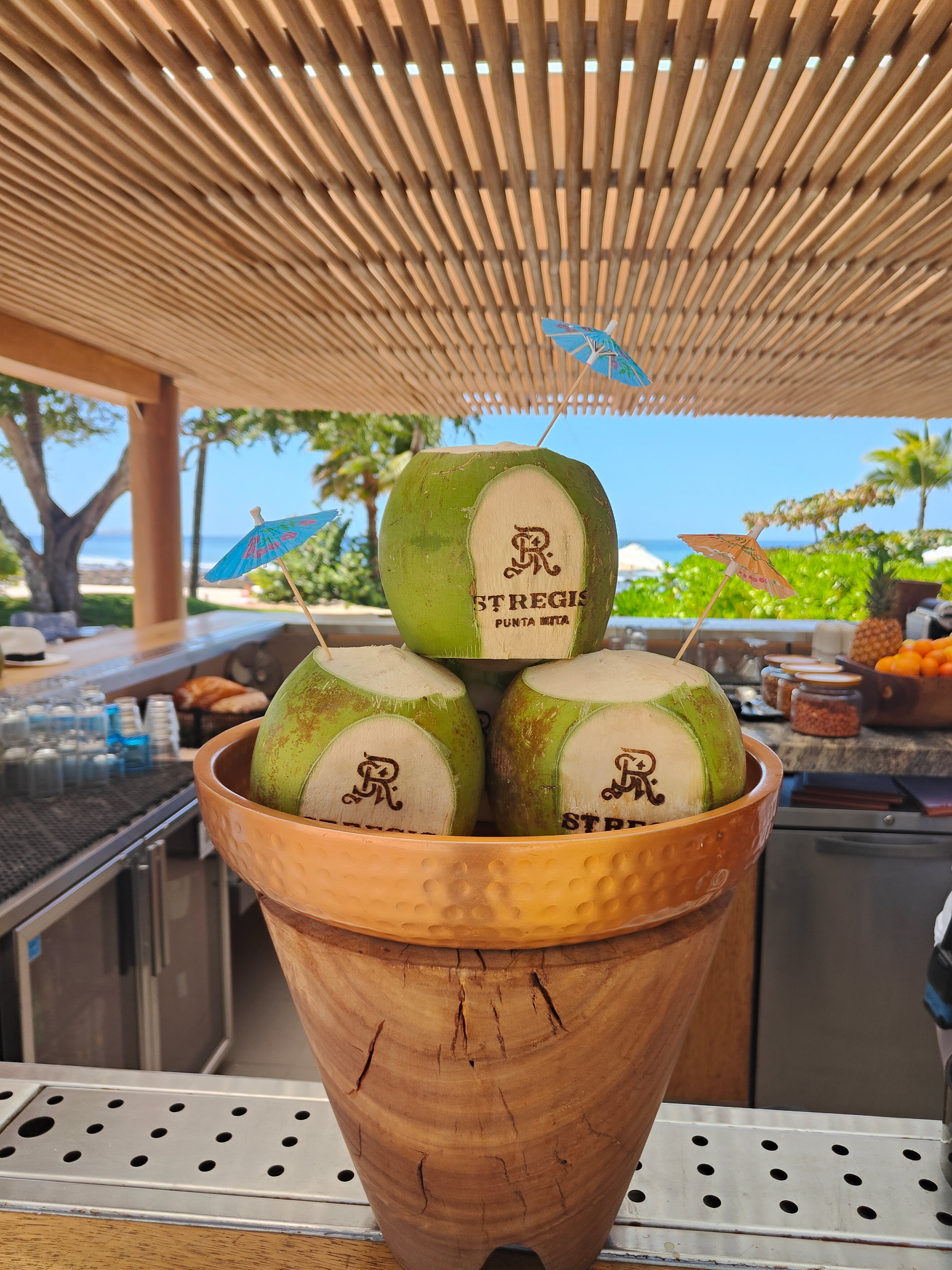 Coconuts with a brand logo for St. Regis in a wooden bowl on a outdoor kitchen counter.