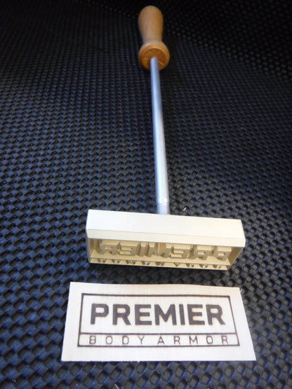 Metal stamp with wooden handle and 'Premier Body Armor' label on a textured black surface