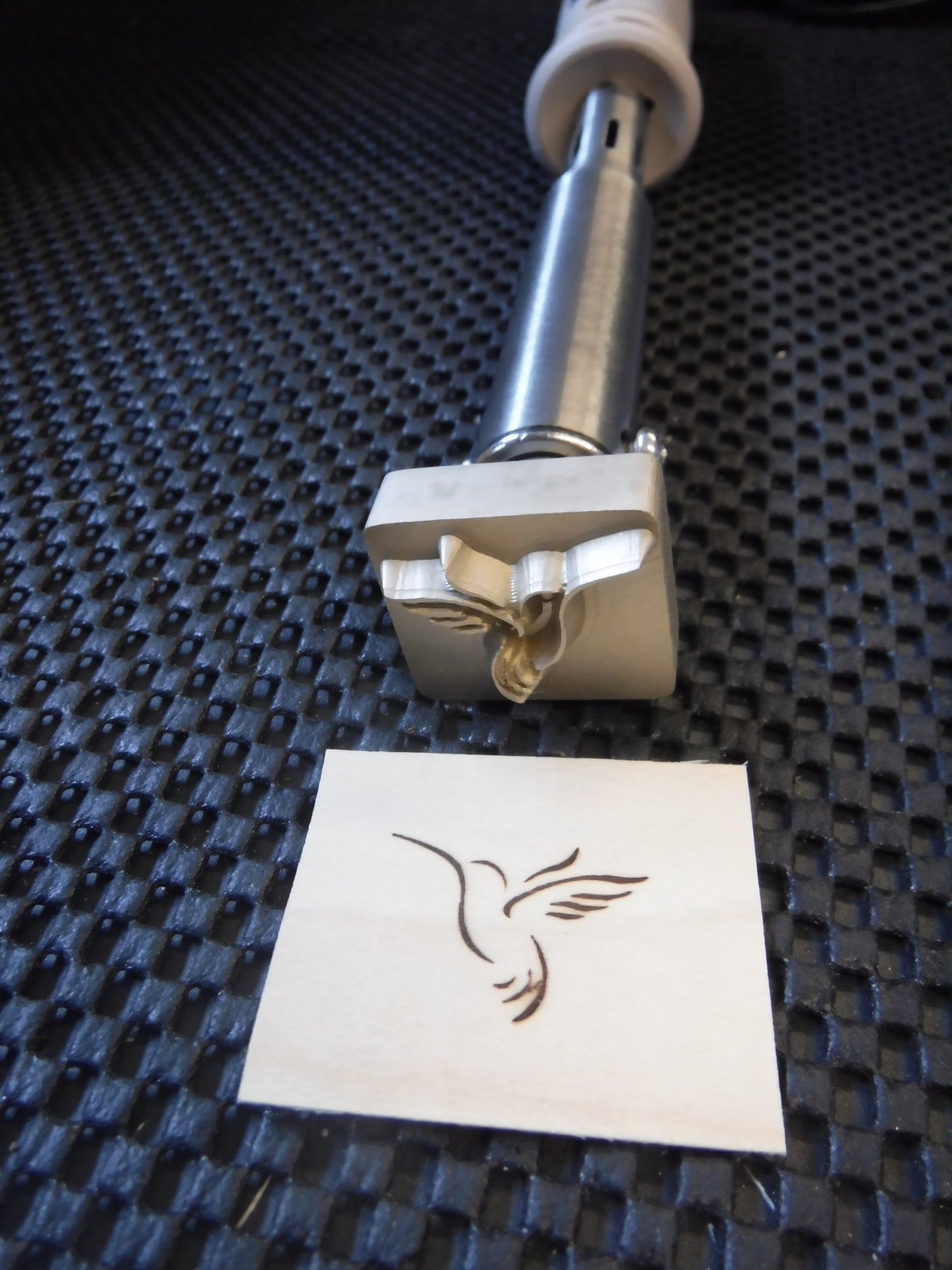 Brass Electric Branding Iron of a humming bird design on a textured black surface